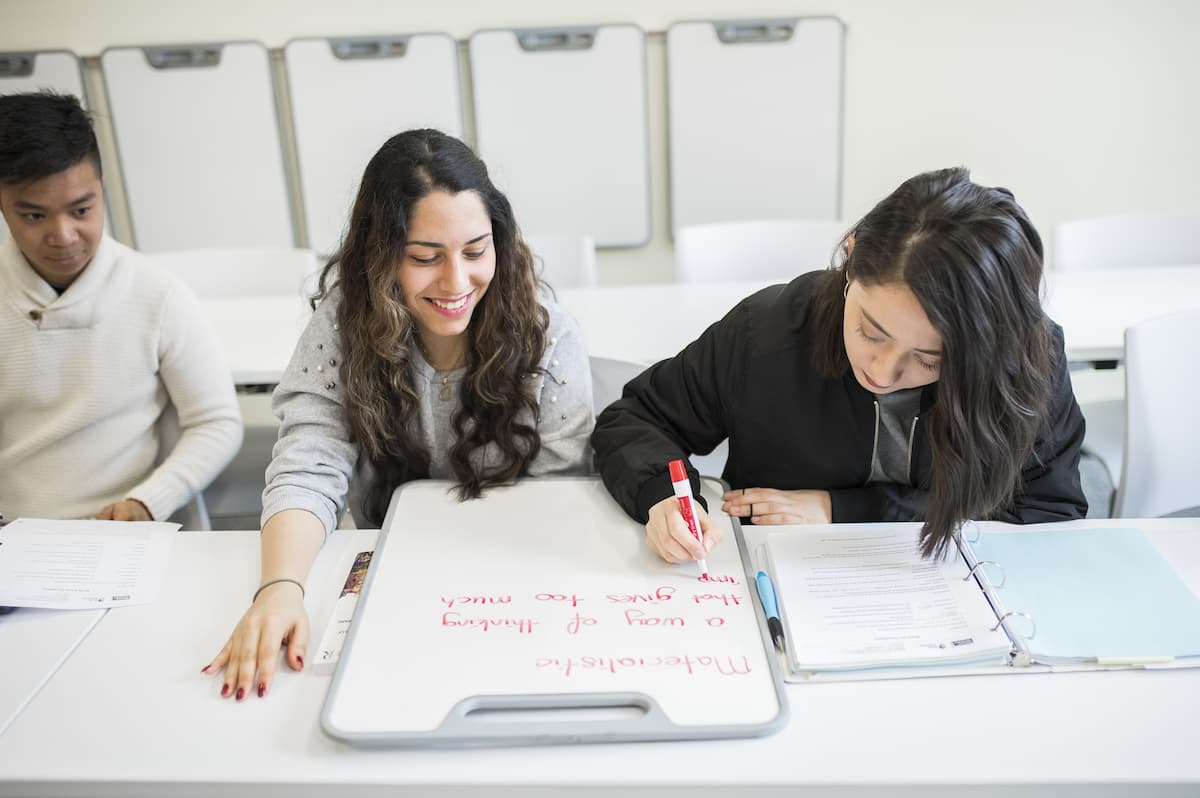 Two students taking turns writing on a small whiteboard